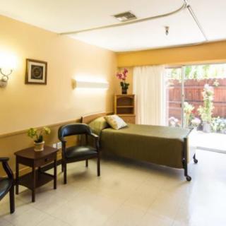 A well-lit hospital room with a bed, chairs, and a window overlooking greenery.