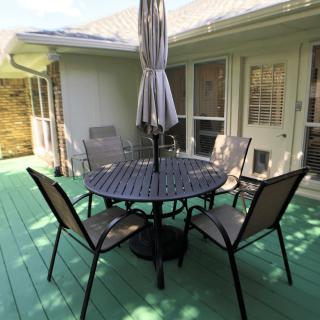 A patio set with a round table, four chairs, and an umbrella on a green deck.
