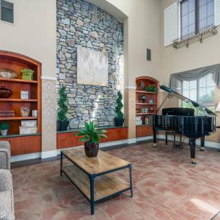 A spacious living room with a grand piano, stone accent wall, and decorative shelving.