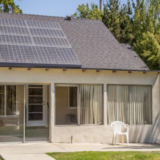A house with solar panels on the roof and a small patio area in the backyard.