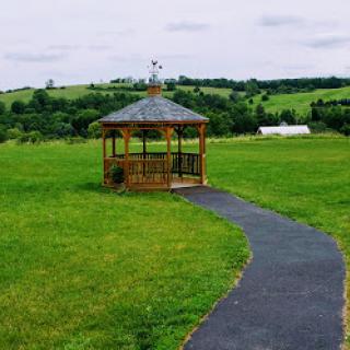 A scenic view of a wooden gazebo surrounded by lush green fields and a winding pathway.