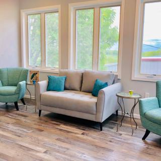 A modern living room with a beige sofa and teal armchairs, complemented by wooden flooring and large windows.