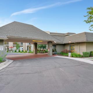 A modern building's entrance with a paved driveway and landscaped surroundings under a clear blue sky.