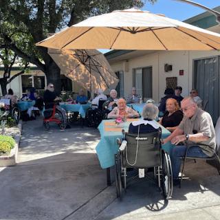 Elderly residents enjoying a lively outdoor gathering under sun umbrellas.