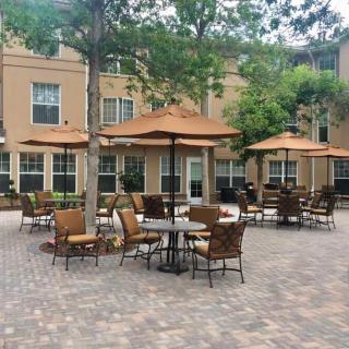 Outdoor patio area with tables, chairs, and umbrellas surrounded by buildings and trees.