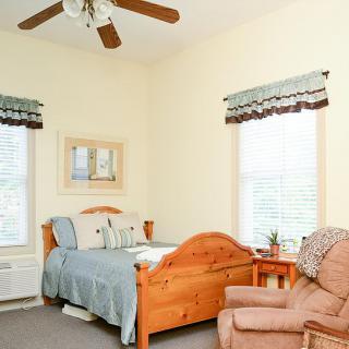 A cozy bedroom with a wooden bed, armchair, and ceiling fan.