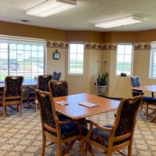 A cozy dining area with tables and chairs, featuring large windows and decorative lighting.