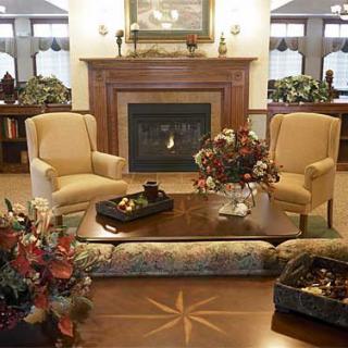 A cozy living room with a central fireplace, flanked by armchairs and a coffee table adorned with floral arrangements.
