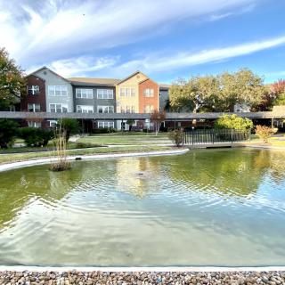 A scenic view of a modern building overlooking a tranquil pond surrounded by trees.