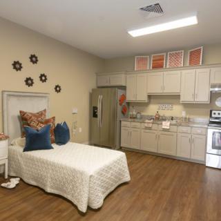 A cozy studio apartment with a kitchenette and a bed, featuring warm decor.