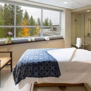 A serene spa room with a massage table and large windows letting in natural light.