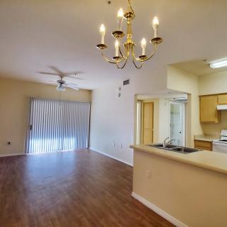 A spacious apartment with an open floor plan, featuring a living room and kitchen area with hardwood floors and a chandelier.