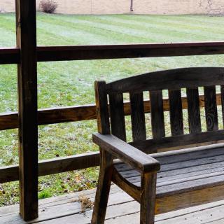 A wooden bench on a porch overlooking a neatly trimmed lawn.