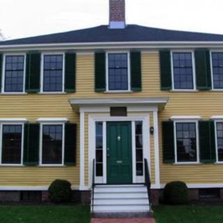 A traditional colonial-style house with yellow siding and green shutters.
