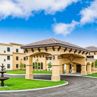Elegant entrance of a modern building with landscaped grounds and a fountain.