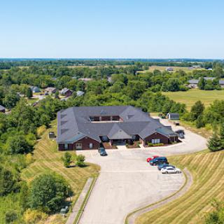 Aerial view of a modern building surrounded by lush greenery and a spacious parking lot.