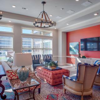 A stylish and well-lit living room featuring a cozy seating arrangement, vibrant decor, and large windows.