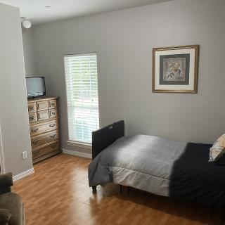 A cozy bedroom with a single bed, dresser, and a TV, featuring gray walls and hardwood flooring.