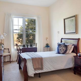 A cozy bedroom with a single bed, large window, and elegant wooden furniture.
