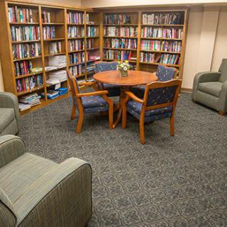 A cozy library seating area with bookshelves, a round table, and comfortable chairs.