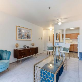 A modern living space with stylish furnishings, featuring blue accents and an open floor plan connecting the living room, dining area, and kitchen.