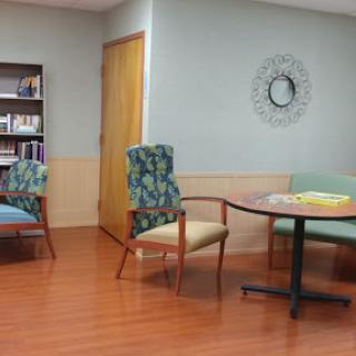 A cozy waiting room with colorful chairs and a bookshelf, featuring warm wooden flooring.