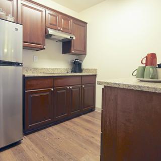 A modern kitchen with wooden cabinets, stainless steel appliances, and a countertop featuring a coffee maker and teapot.