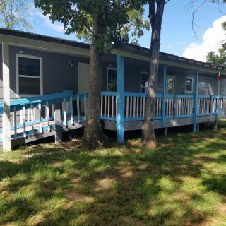 A blue house with a wooden porch surrounded by trees on a sunny day.