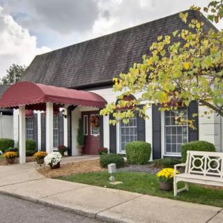 A quaint building with a red canopy entrance, surrounded by landscaping, trees, and flowers.