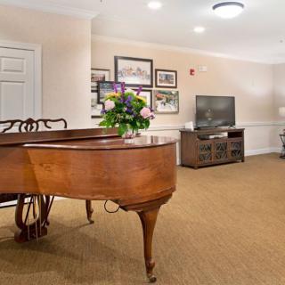 A cozy living room features a grand piano, television, and beautiful floral arrangement.
