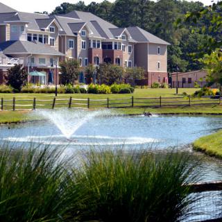 A scenic view of an apartment complex with a pond and water fountain in the foreground.
