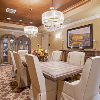 An elegantly designed dining room featuring a large table, upholstered chairs, and two chandeliers.