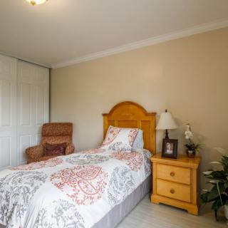 A cozy bedroom featuring a single bed, nightstand with a lamp, and a comfortable chair.
