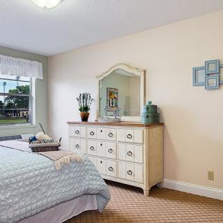 A cozy bedroom featuring a dresser with a mirror, a neatly made bed, and decorative elements near the window.