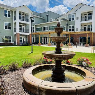 A scenic view of a residential building with a central fountain and landscaped garden.