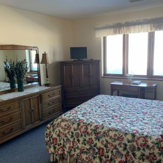 A cozy bedroom featuring a floral bedspread, wooden furniture, and a sunny window view.