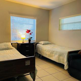 A cozy bedroom with two single beds and a nightstand between them, featuring a lamp and a window with blinds.