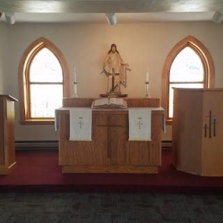 A serene view of an altar inside a church with wooden decor and arched windows.