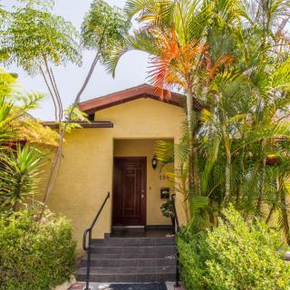 A tropical house entrance surrounded by lush greenery and palm trees.
