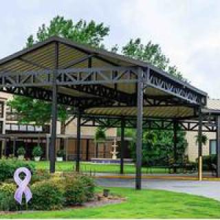 A modern canopy structure in front of a building, surrounded by landscaping and greenery.