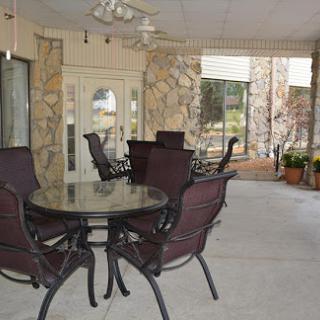 A cozy outdoor seating area featuring a glass table and metal chairs, surrounded by stone walls and plants.