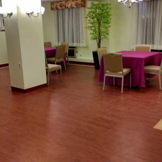 An empty conference or dining room with tables and chairs arranged around the space, featuring a wooden floor and decorative plants.