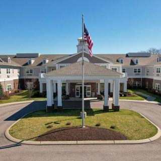 A large residential building with an American flag at the entrance, surrounded by landscaped grounds and a circular driveway.