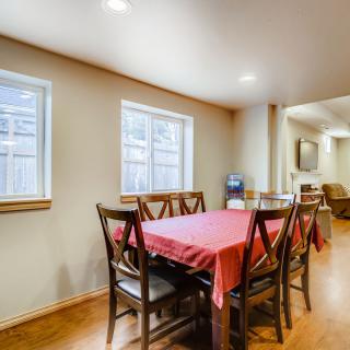 A cozy dining room with a red tablecloth and wooden chairs, featuring natural light from two windows.