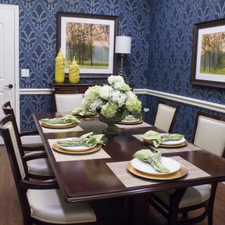 Elegant dining room with blue wallpaper, featuring a dark wood table set with green napkins and floral centerpiece.