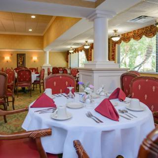 An elegant restaurant dining room with neatly set tables and red cushioned chairs.