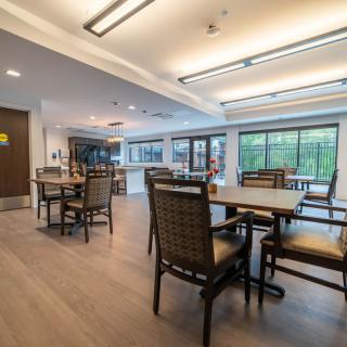A modern dining area with tables and chairs, well-lit with large windows.