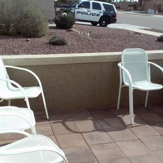 A residential patio with white chairs overlooks a driveway with a parked police car.