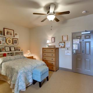 A cozy bedroom with a comfortable bed, wooden dresser, and ceiling fan, decorated with various framed artworks.