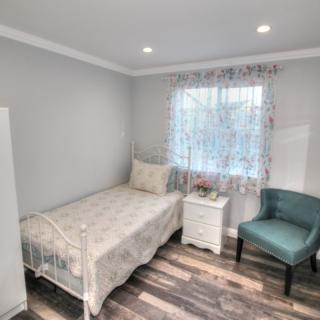 A small, modern bedroom with a single bed, nightstand, and a teal chair.